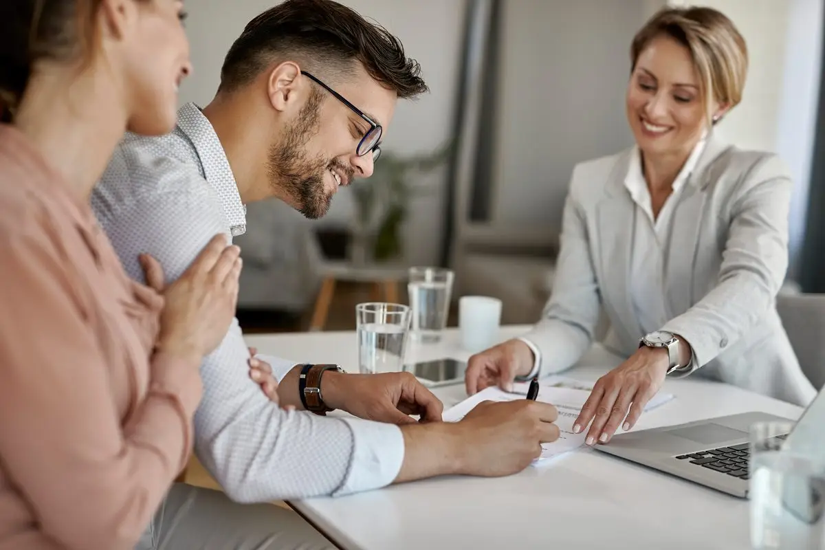 An adviser sitting between a couple at a table helping them go through paperwork