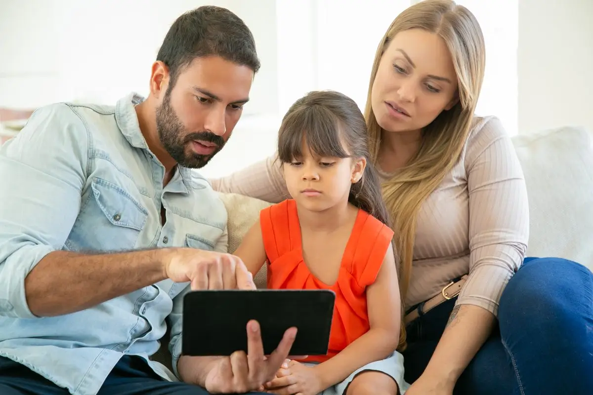A mother and father with their young daughter looking at a tablet together
