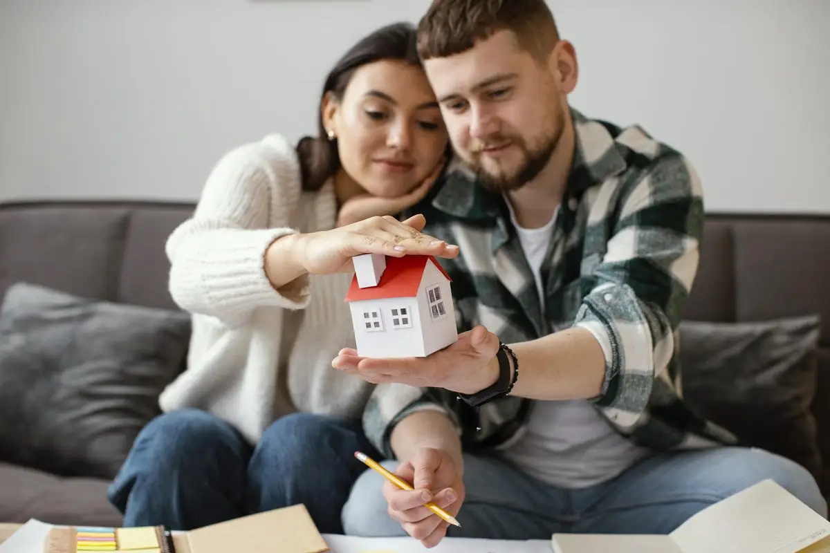 A couple sitting on their sofa holding a small model house while they plan