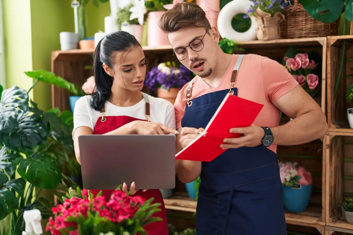 Two small business owners working on a laptop and ledger in their shop