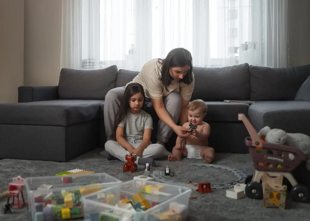 A mother playing with two young children on the living room floor at home