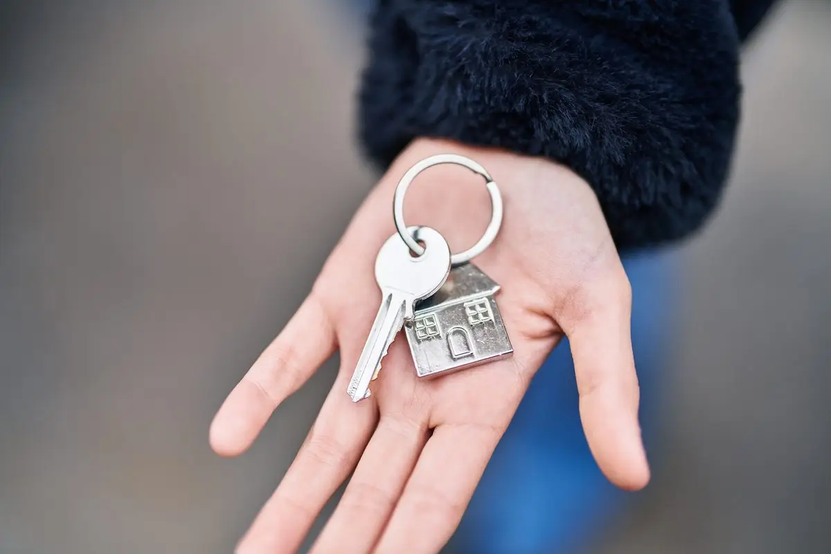 A hand holding house keys with a small house-shaped key ring