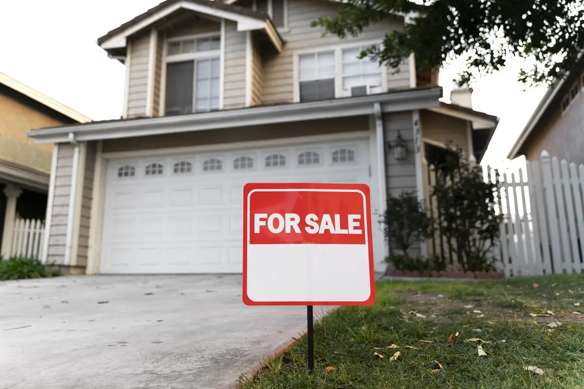 A for sale sign on the lawn in front of a suburban house