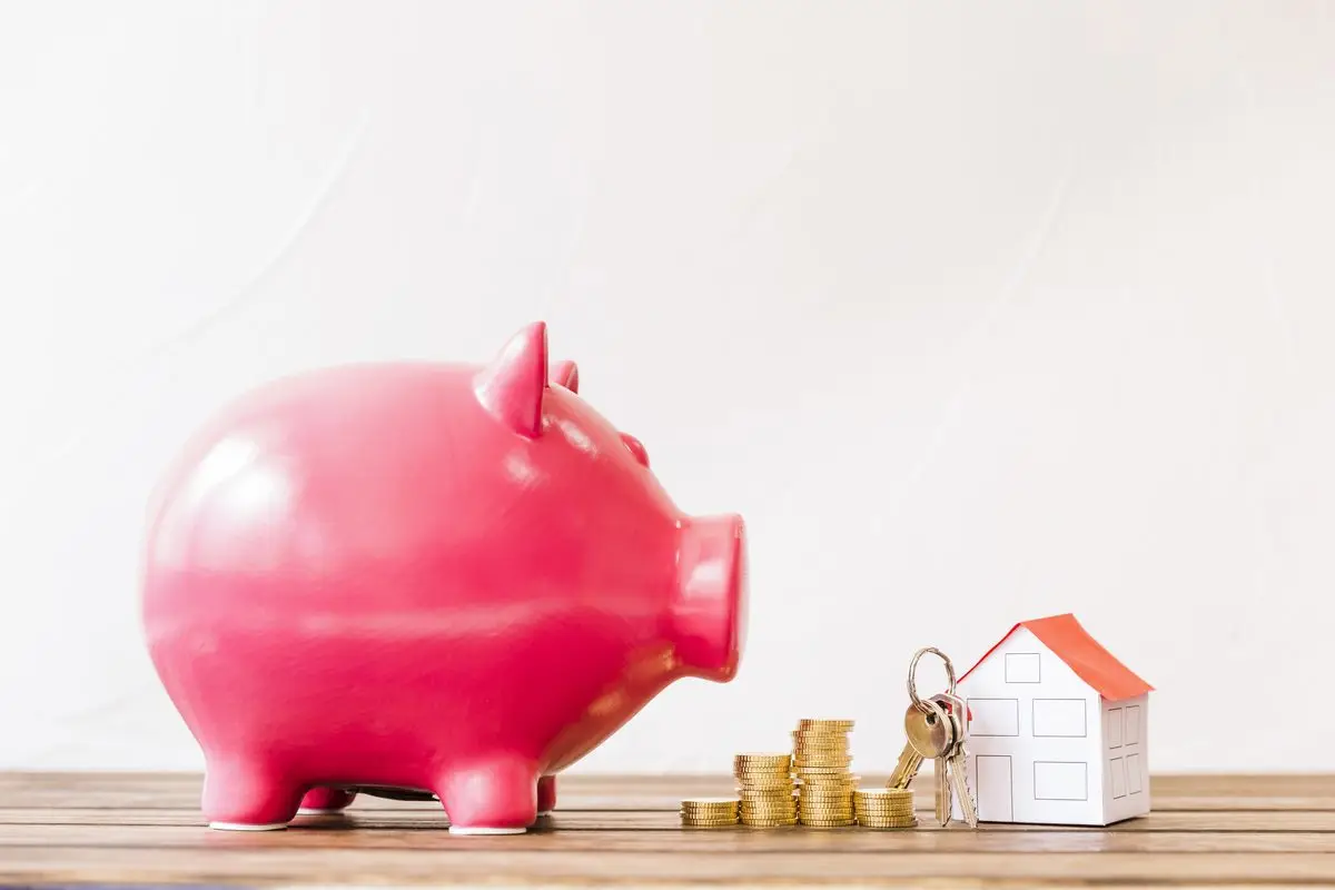 A piggy bank beside stacked coins and a small house with a key