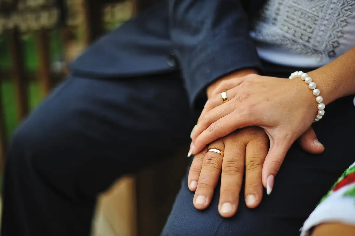 A married couple resting their hands together, both wearing wedding rings