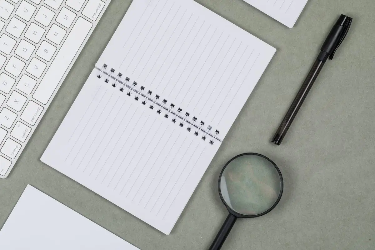 A magnifying glass resting on a notebook beside a keyboard