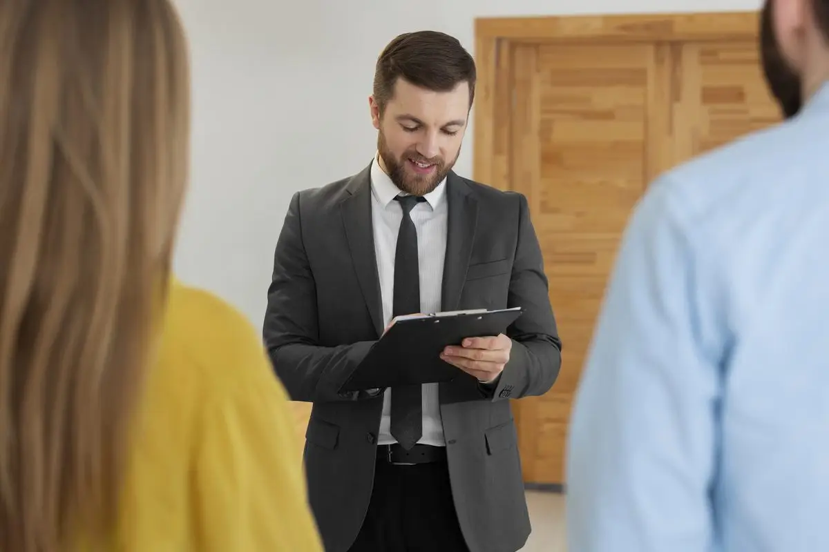 A real estate professional with a clipboard assessing a property while a couple looks on