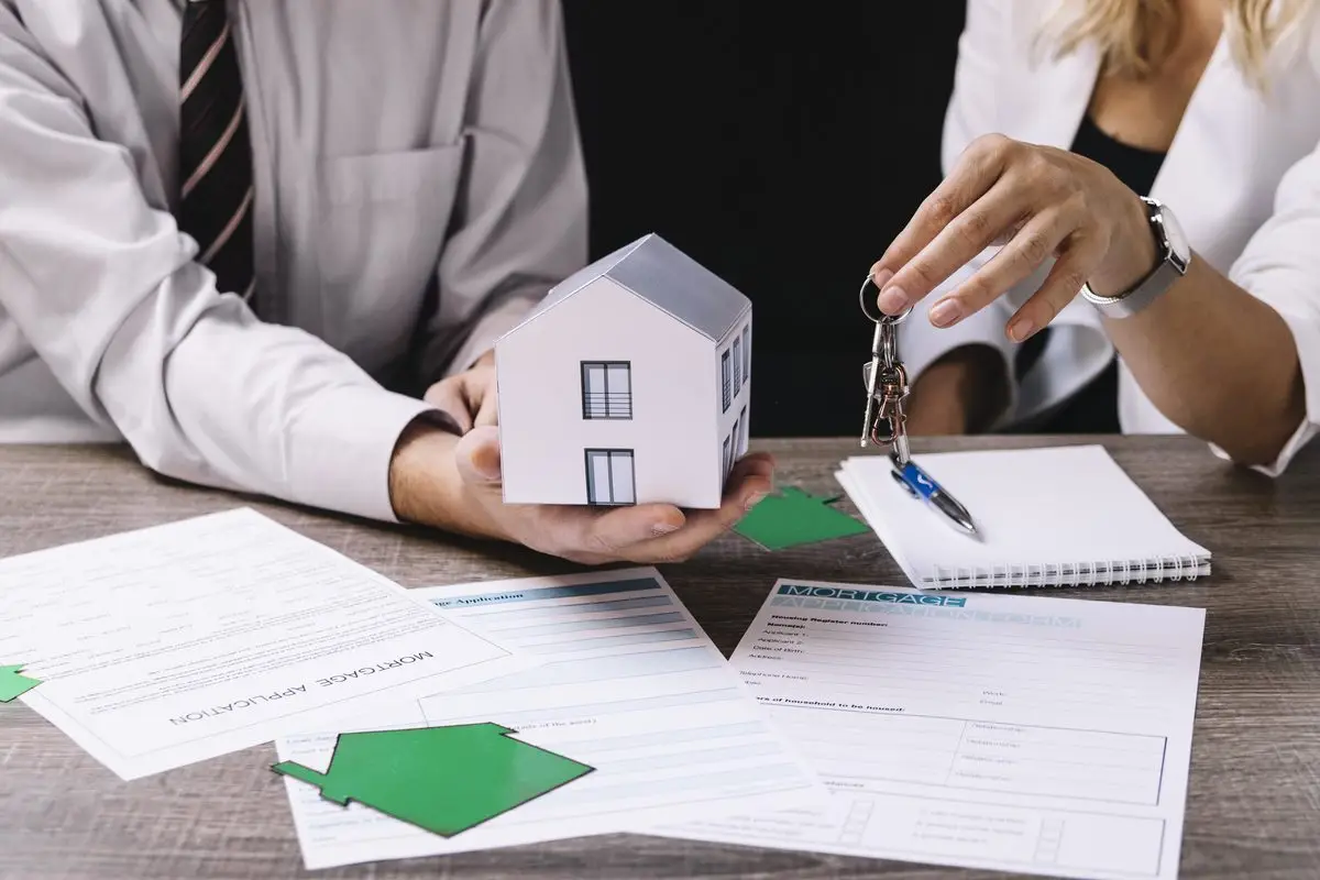 A small model house and keys on a table beside property paperwork