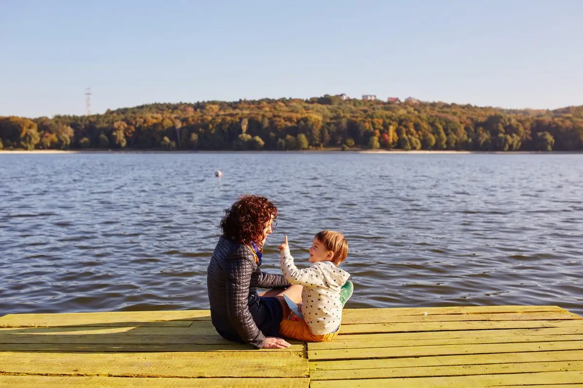 A mother and her young son sitting on a lakeside dock playing together