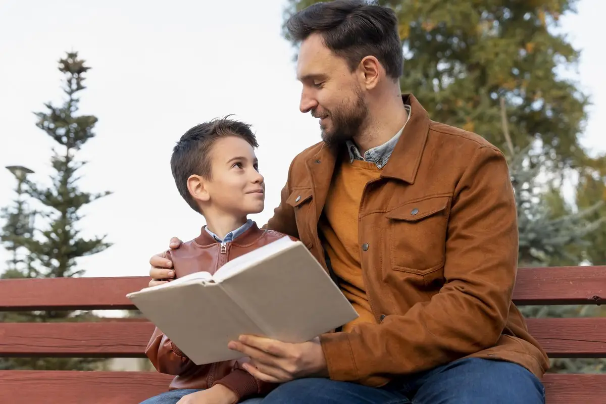 A father reading a book with his son on a park bench
