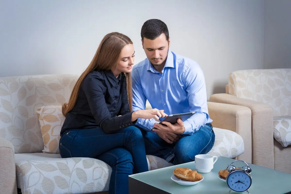 A couple sitting side by side on a sofa looking at a tablet