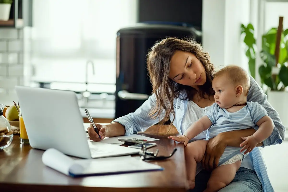 A mother working at her kitchen table while holding her baby