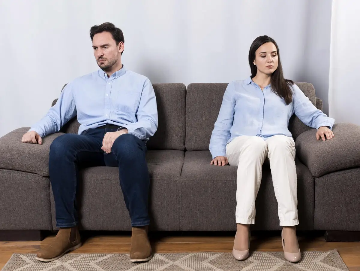 A married couple sitting back to back on a sofa after separating