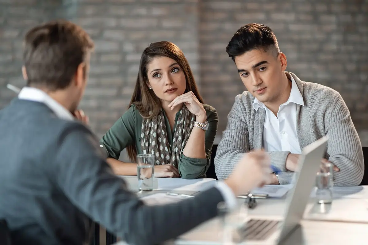 Two spouses sitting side by side with an adviser going over paperwork together