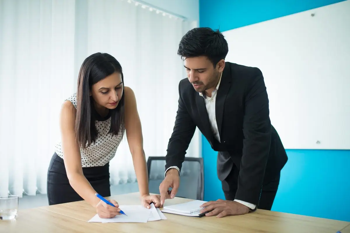 Two people leaning over a table to complete and sign paperwork