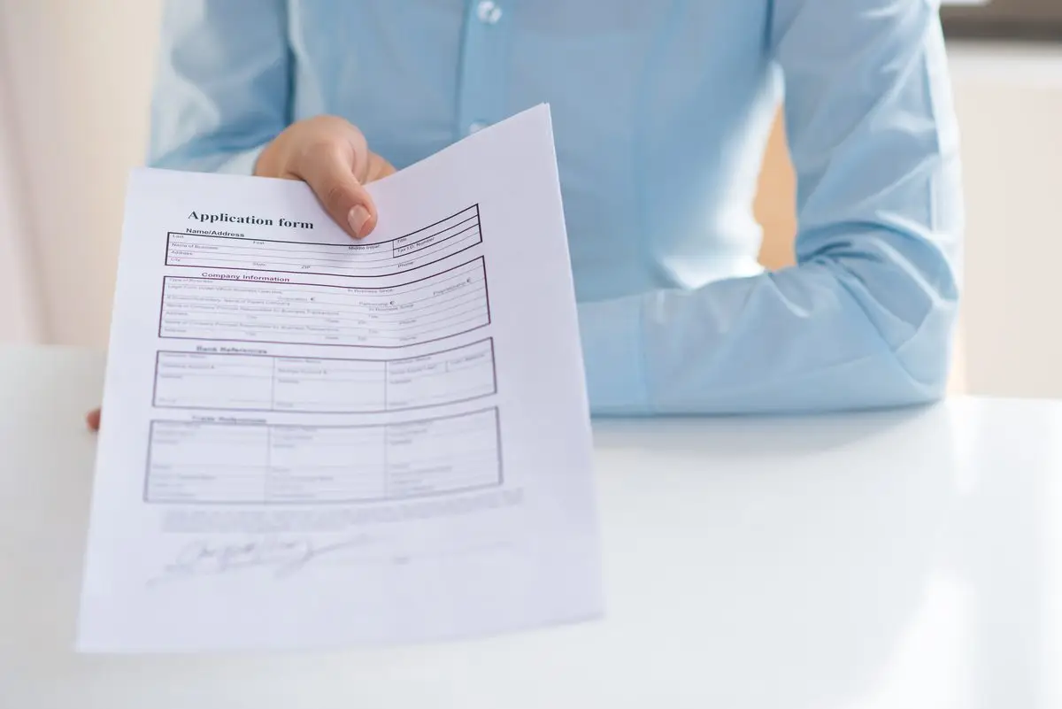 A hand holding out a completed application form across a desk