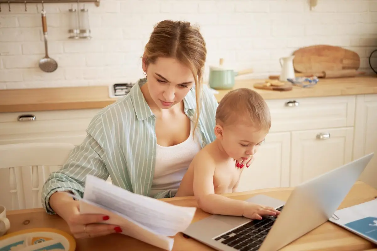 A parent at the kitchen table going through bills and paperwork with a young child on their lap